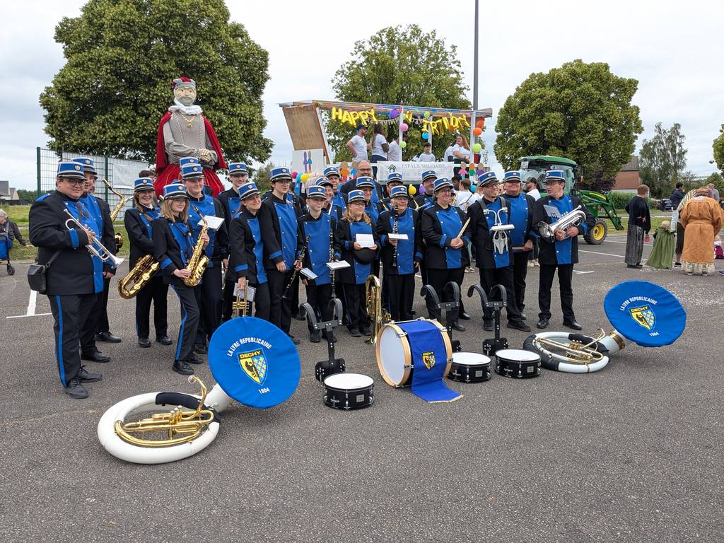 Les musiciens de l'Harmonie de Dechy en uniforme bleu et noir, devant un char décoré lors d'un cortège.